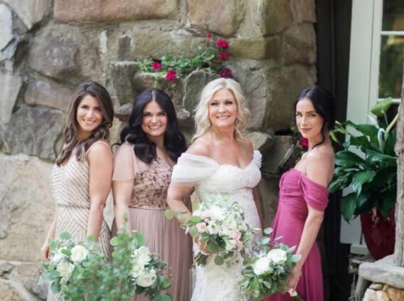 bride and bridesmaids standing next to stone wall