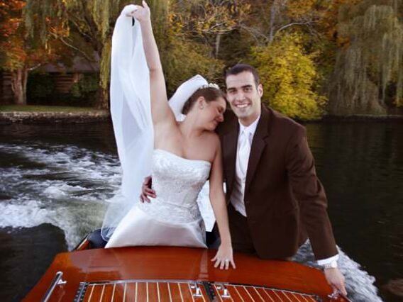 bride with her hand up and groom riding on a boat on the lake