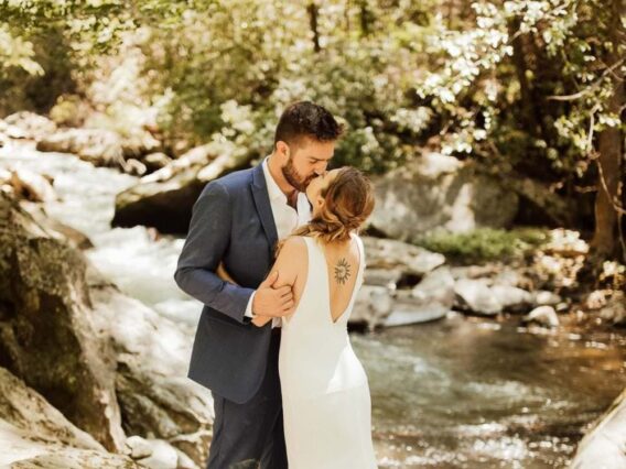 bride and groom kissing next to river